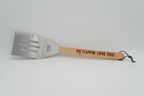 Barbecue spatula with wooden handle and engraved text on a gray background