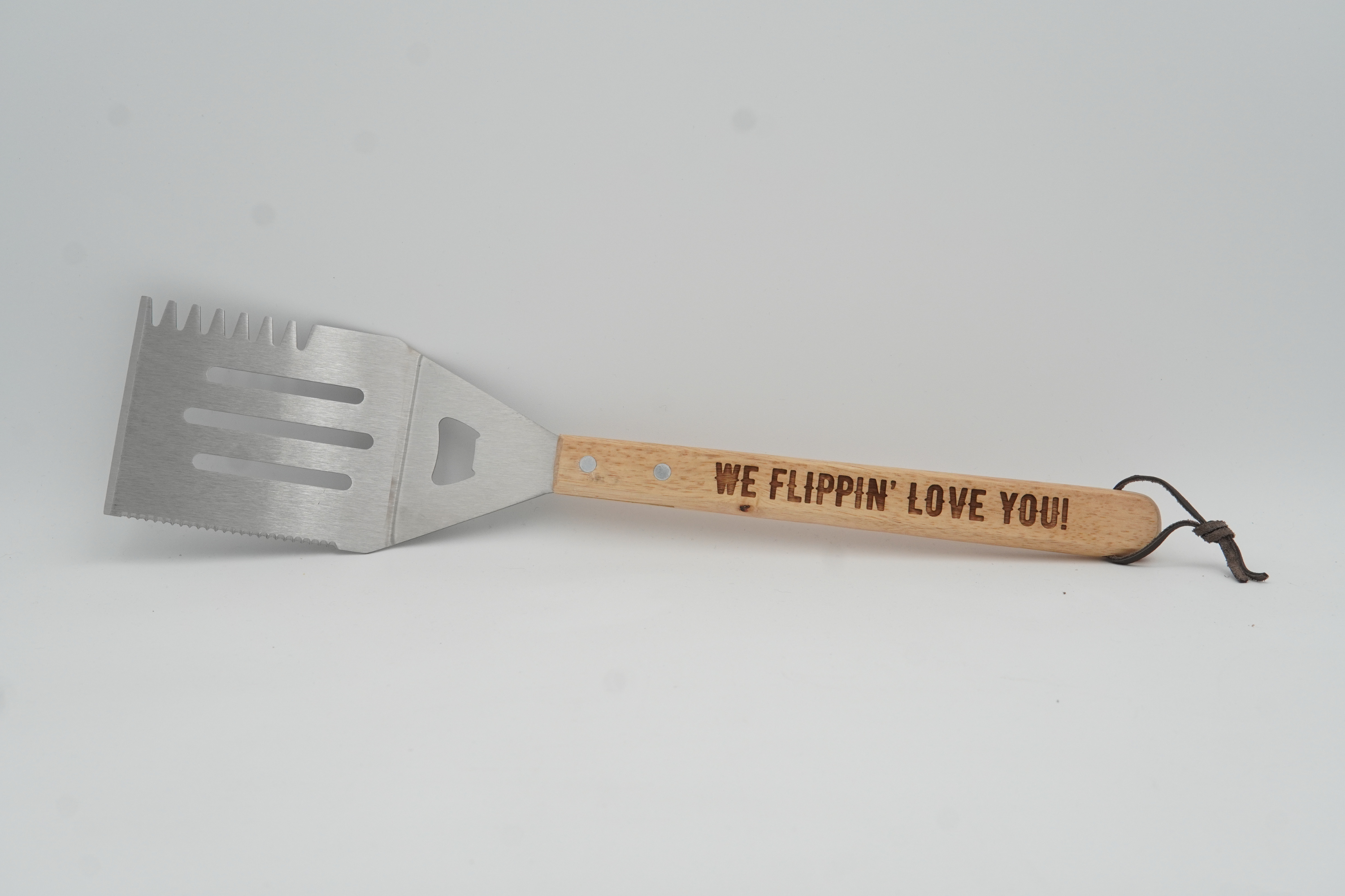 Barbecue spatula with wooden handle and engraved text on a gray background