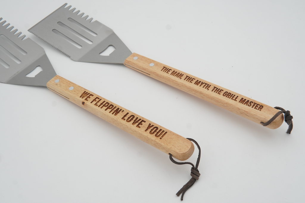 Two spatulas with wooden handles and engraved text on a light gray background