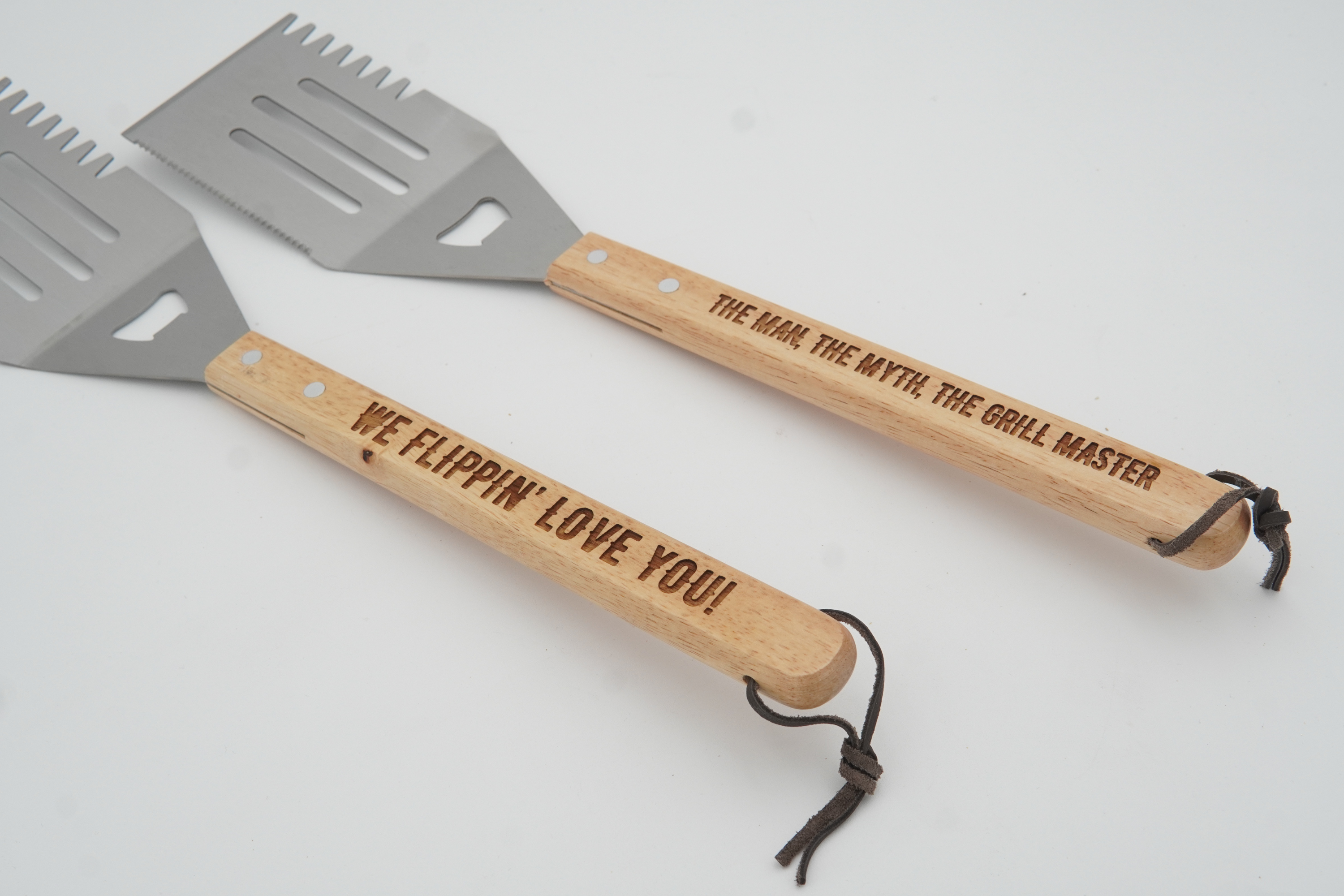 Two spatulas with wooden handles and engraved text on a light gray background