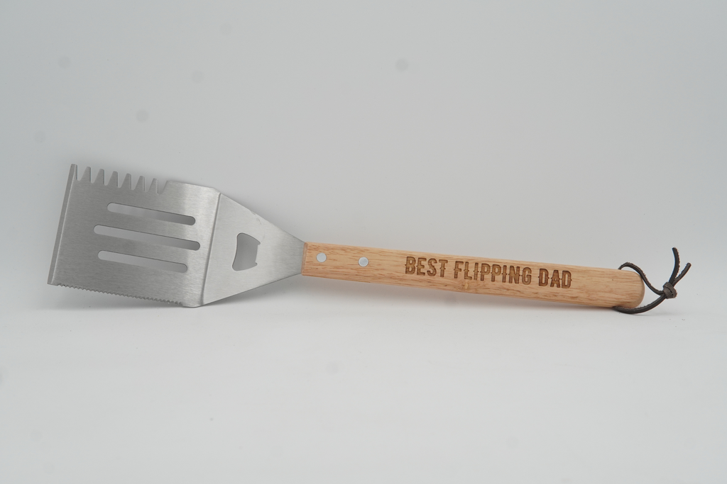 Grill spatula with wooden handle and engraved text on a light gray background
